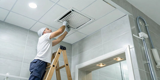 A person mounting a new bathroom exhaust fan during a DIY installation.