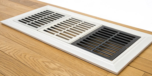 A selection of heating vent covers in various styles and finishes on a wood floor.