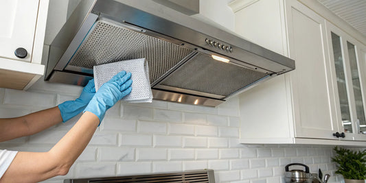A person wearing gloves uses a cloth to clean a greasy kitchen exhaust fan.